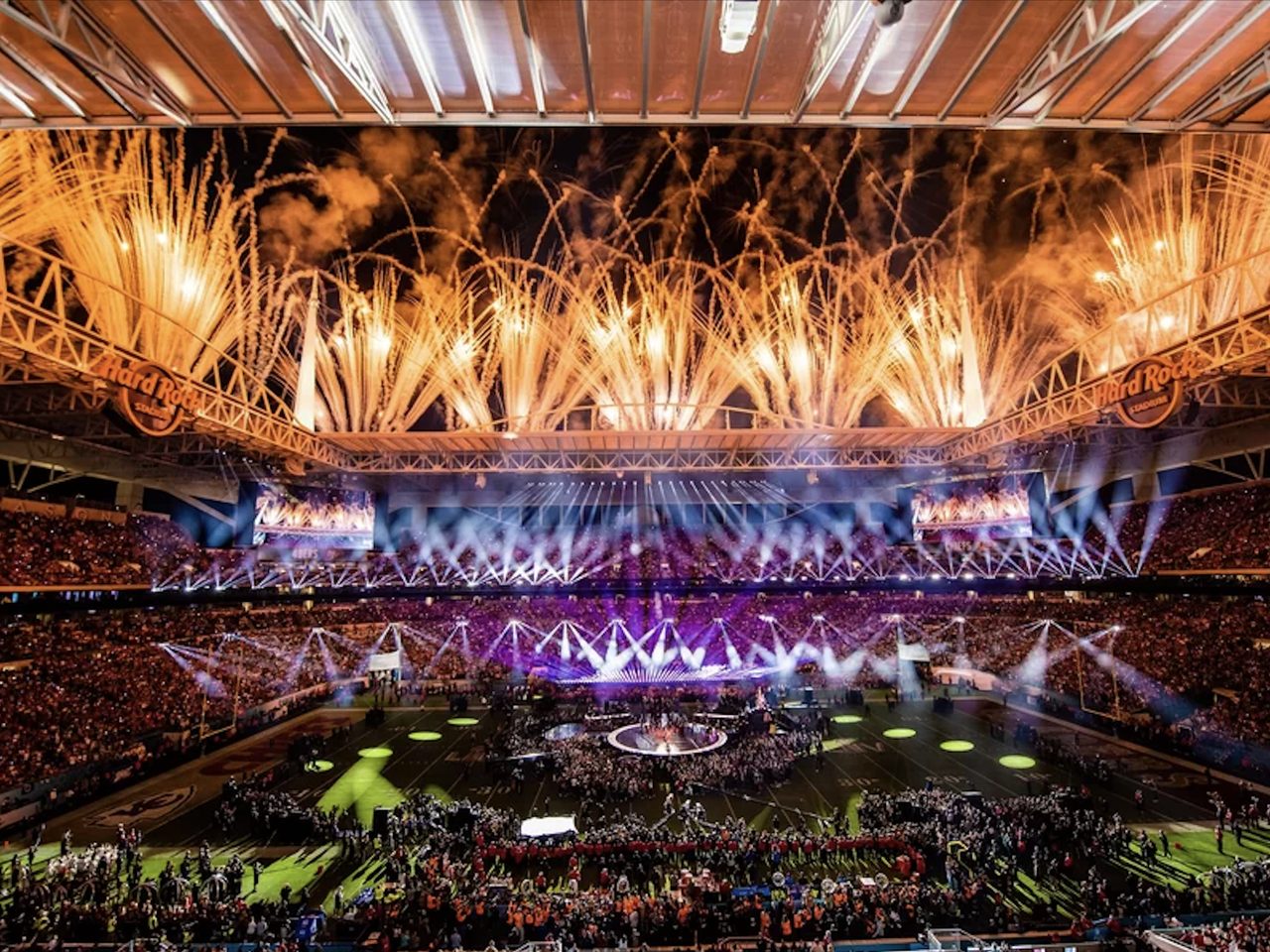 Fireworks and stage lights over a packed stadium during a halftime show at night