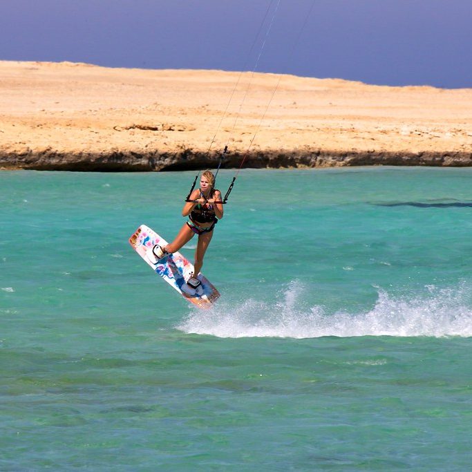 Kitesurfer jumping over turquoise water in front of a desert island near Hurghada